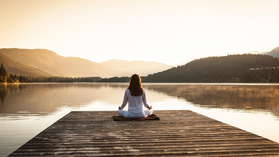 woman practices pranayama and meditation on a dock at sunrise
