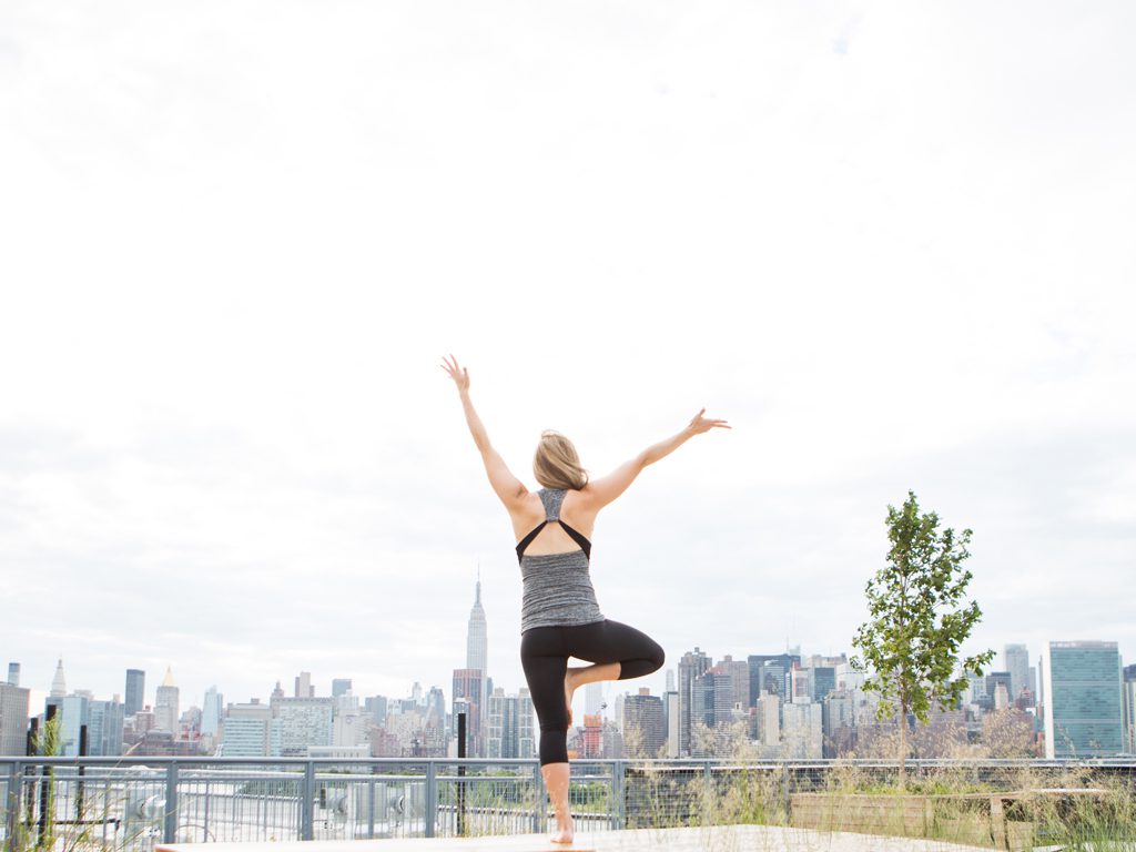 pregnant woman practices tree pose on a deck in New York City