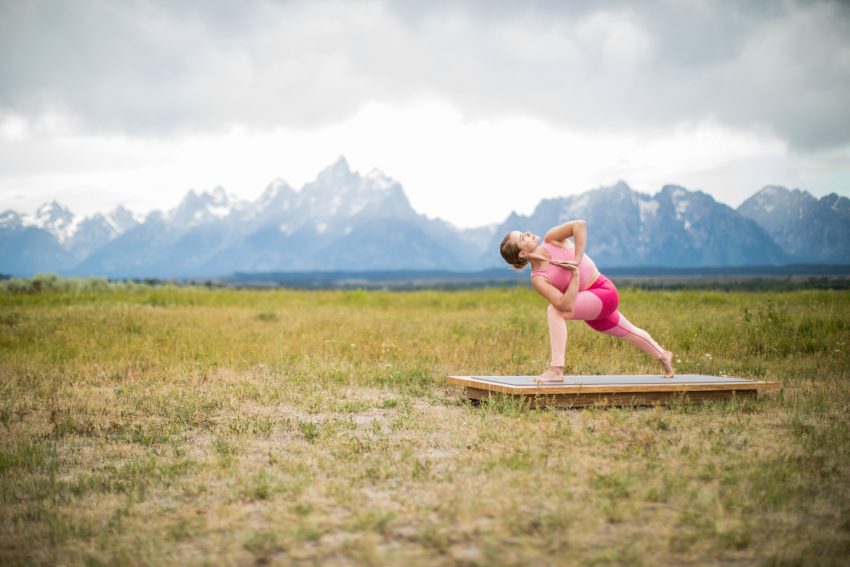 woman practices a twisted lunge on an outdoor yoga platform Grand Teton National Park -yogatoday