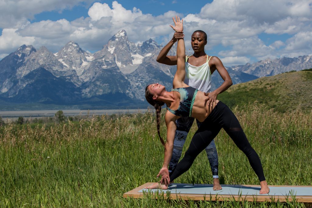 yoga teacher adjust student in triangle pose - yogatoday