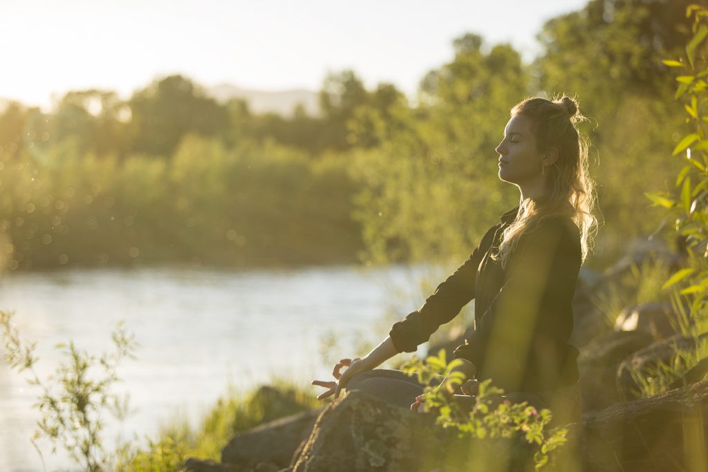 Woman meditates on the back of a river surrounded by greenery