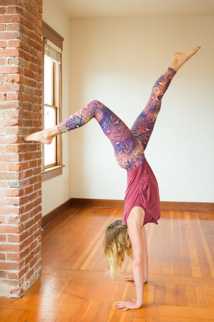 woman practices kicking up into handstand against a wall -yogatoday