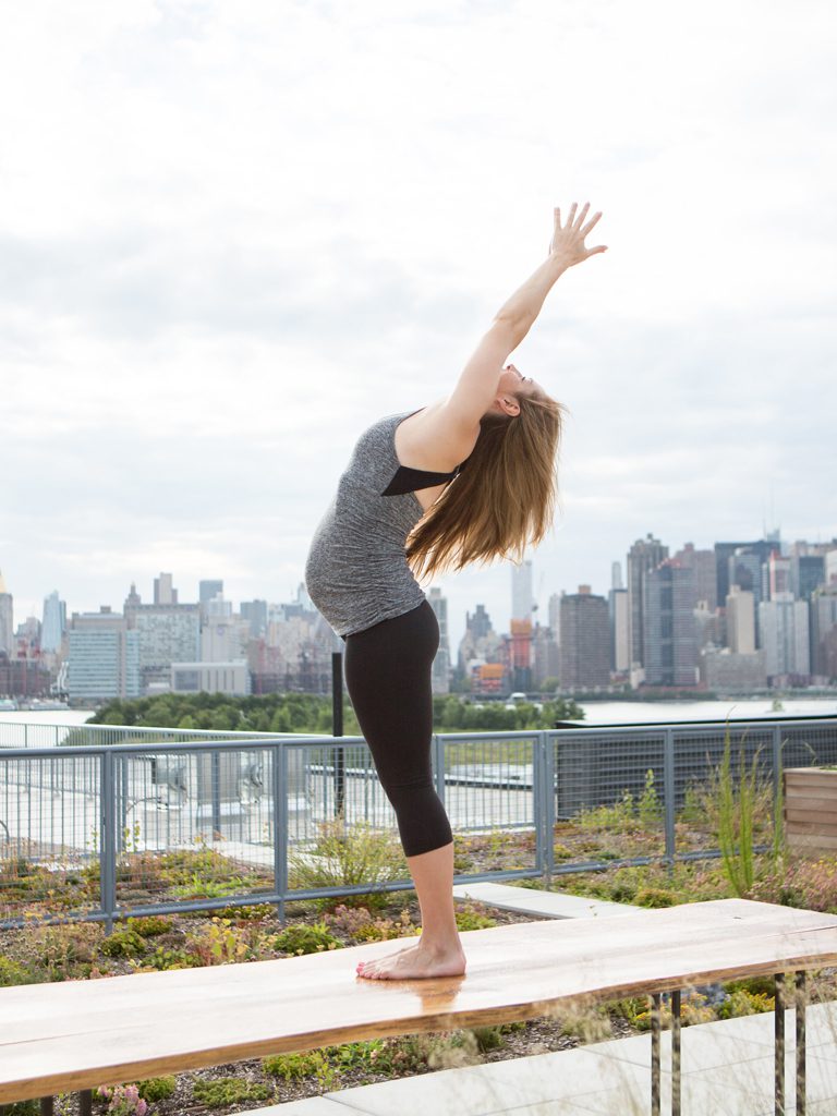pregnant woman practices prenatal yoga on a deck in New York City