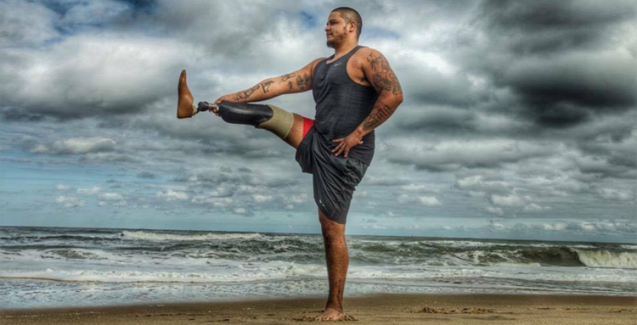 a veteran with a prosthetic leg practices yoga on a beach  