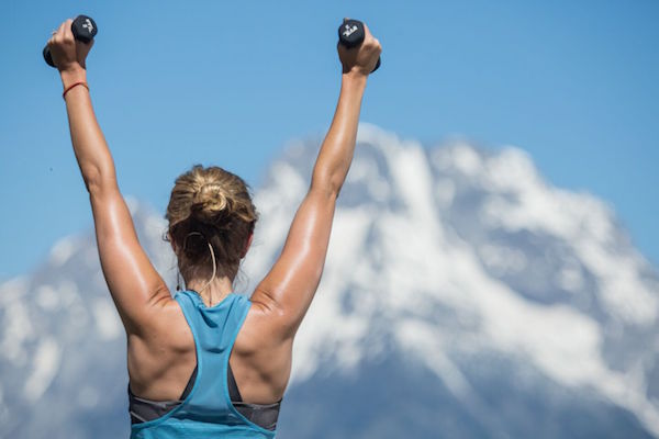 woman lifts weights above her head while practicing yoga sculpt -yogatoday