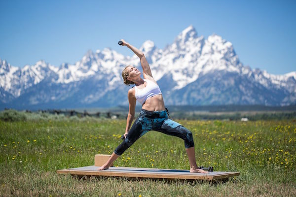 woman practices peaceful warrior pose with weights -yogatoday
