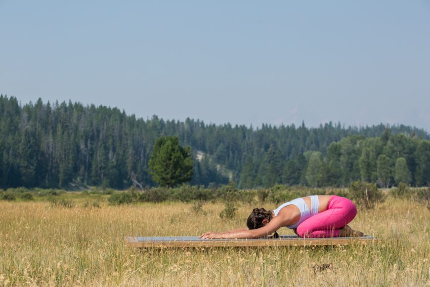 woman practices child's pose on an outdoor yoga platform - yogatoday