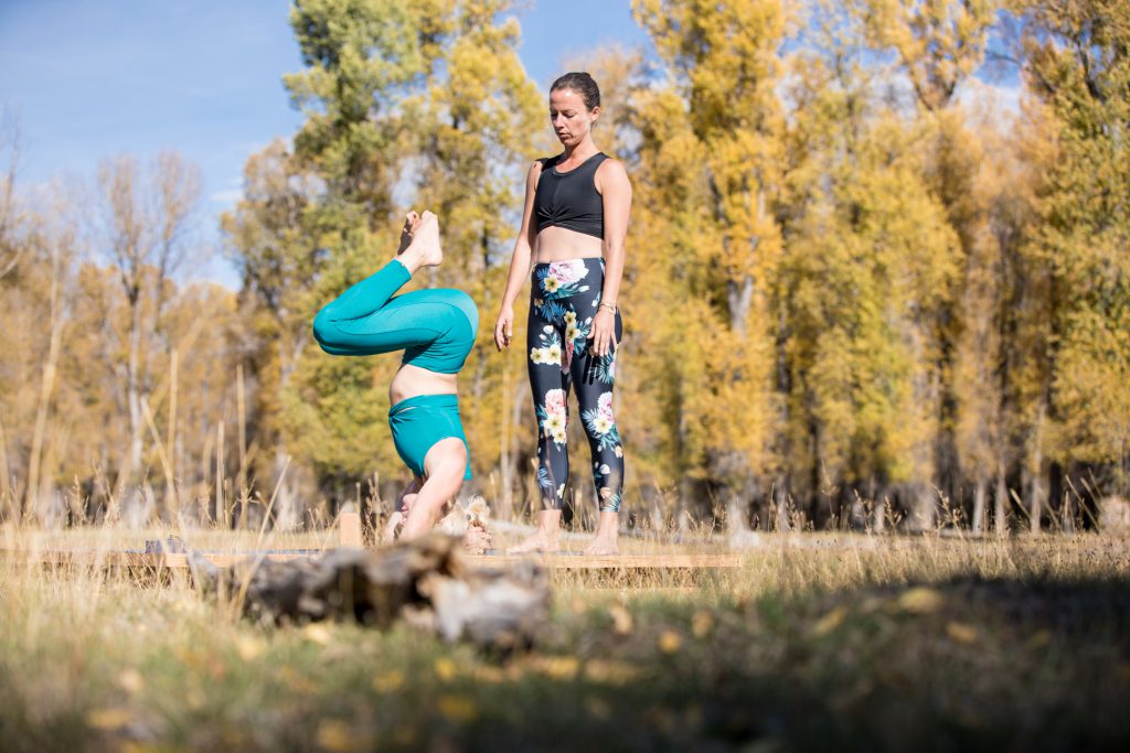 yoga teacher assists a student in pressing up into head stand 