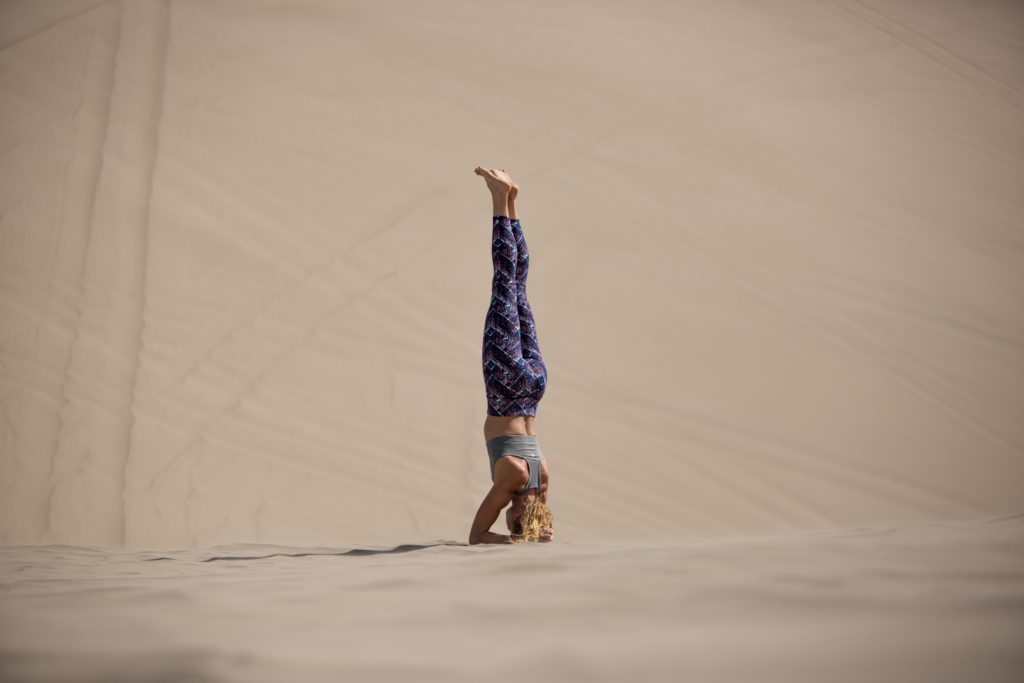 woman practices head stand in desert dunes - YogaToday
