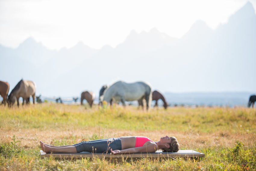 woman practices final resting pose in Grand Teton National Park - YogaToday