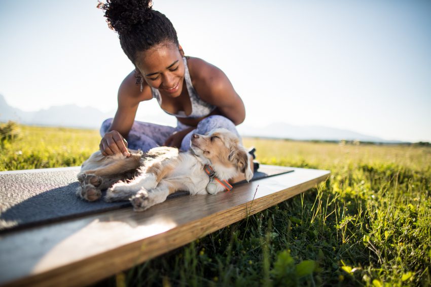 woman practices yoga outside with her dog